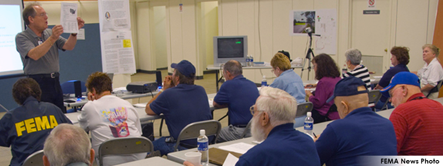 FEMA News Photo - Students listed to instrucor in classroom - Instructor is holding up paper.